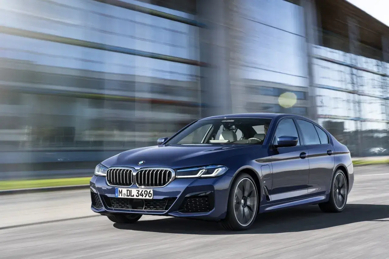 Granatowe BMW G30 540i sunie po drodze, odbijając się w nowoczesnej architekturze.