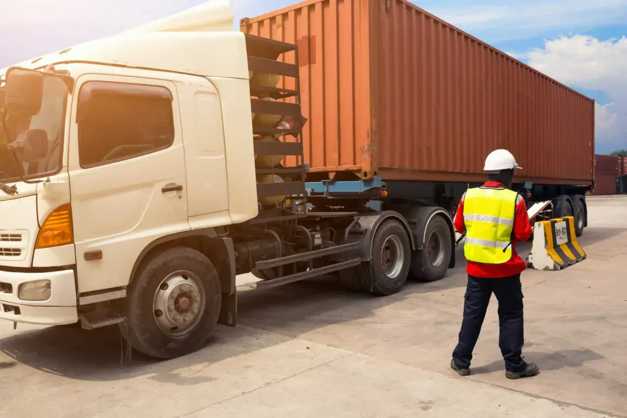 Ein Mann in Warnweste prüft Dokumente neben einem LKW mit Container. Alles bereit für den Frachttransportvertrag.