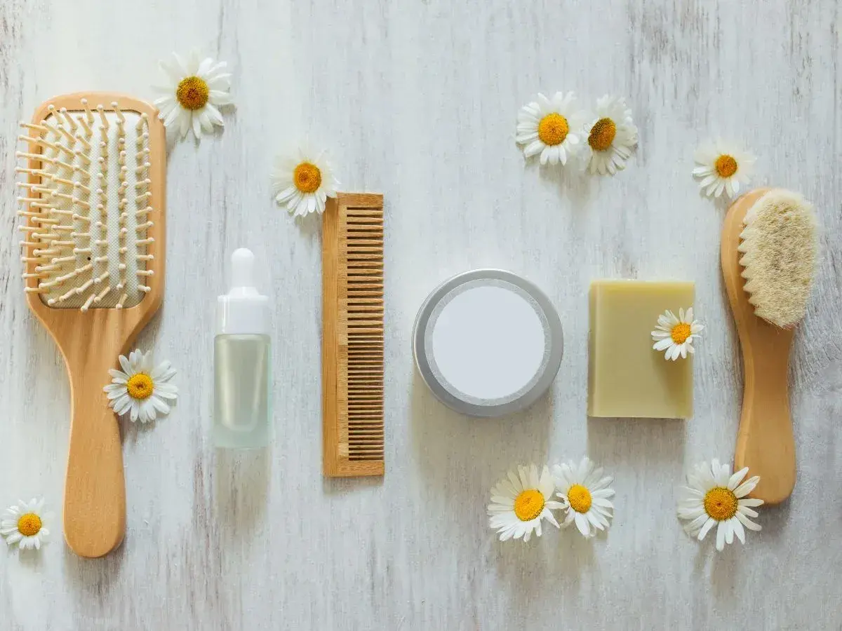 Cepillo, peine, jabón y serum de cuidado personal, todo cruelty free, rodeado de margaritas sobre fondo de madera.