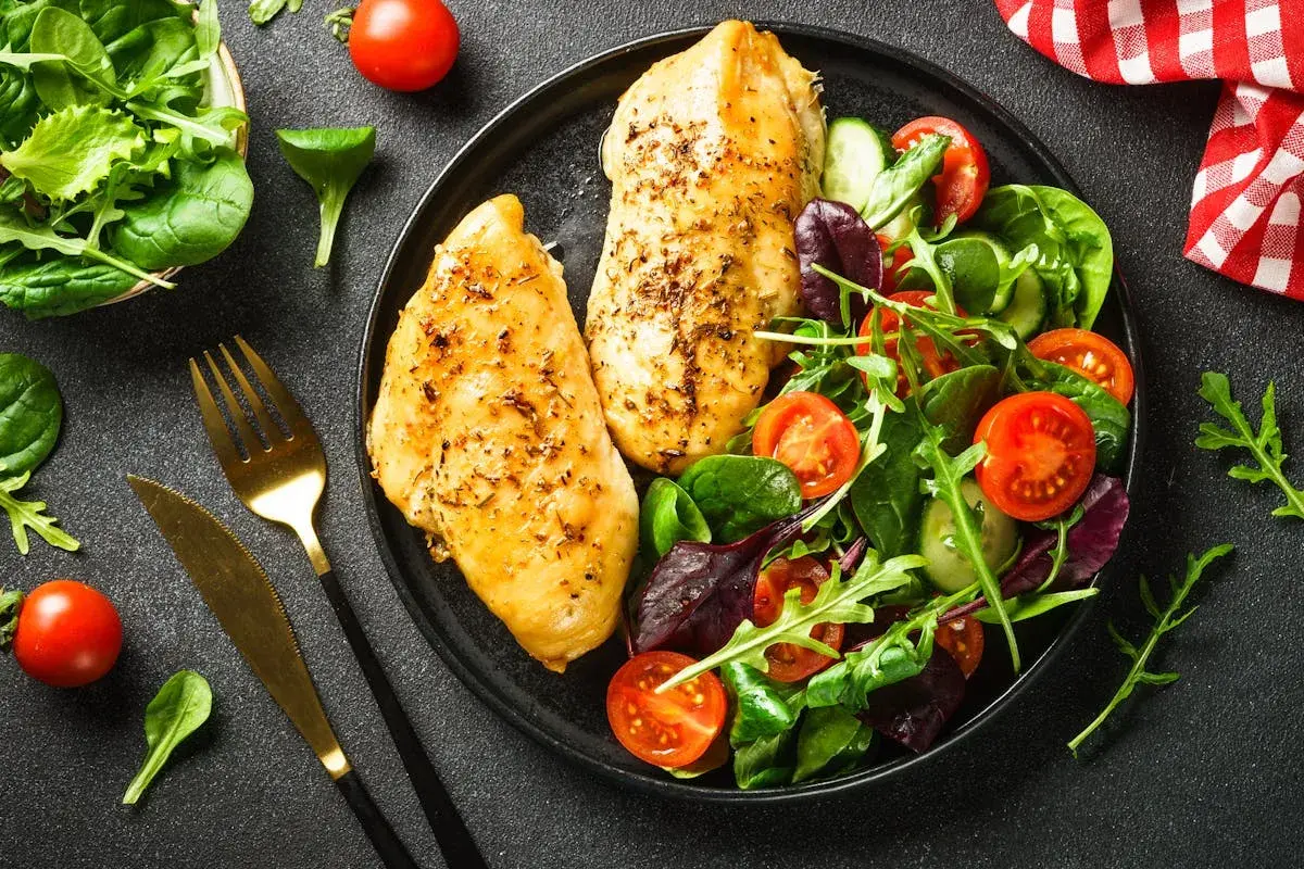 Deux blancs de poulet grillés avec une salade colorée, un repas sain parmi les 10 meilleurs aliments anti-cholestérol.