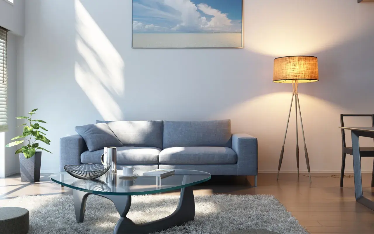 Ein helles Wohnzimmer mit grauem Sofa, Glascouchtisch und einem Bild mit Meerblick. Welche Farbe passt zu grauem Sofa? Hier sehen wir helle Töne, die gut harmonieren.