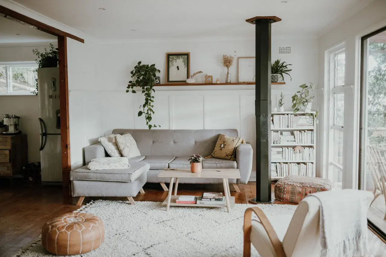 Ett ljust vardagsrum med grå soffa, träbord och bokhylla. Gröna växter och konst ger en känsla av skandinavisk minimalism.