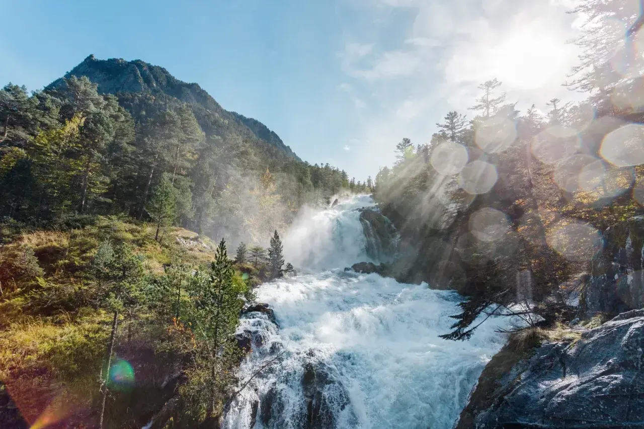 Cascada rugiente en un bosque de montaña, con rayos de sol atravesando la bruma. Un paisaje espectacular que evoca la fuerza de la naturaleza en el **pont de espagne**.