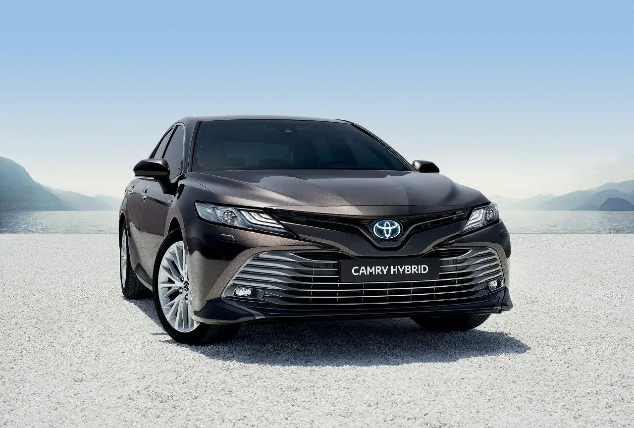 Elegancka, ciemnobrązowa Toyota Camry Hybrid 2020 zaparkowana nad jeziorem, gotowa na podróż.