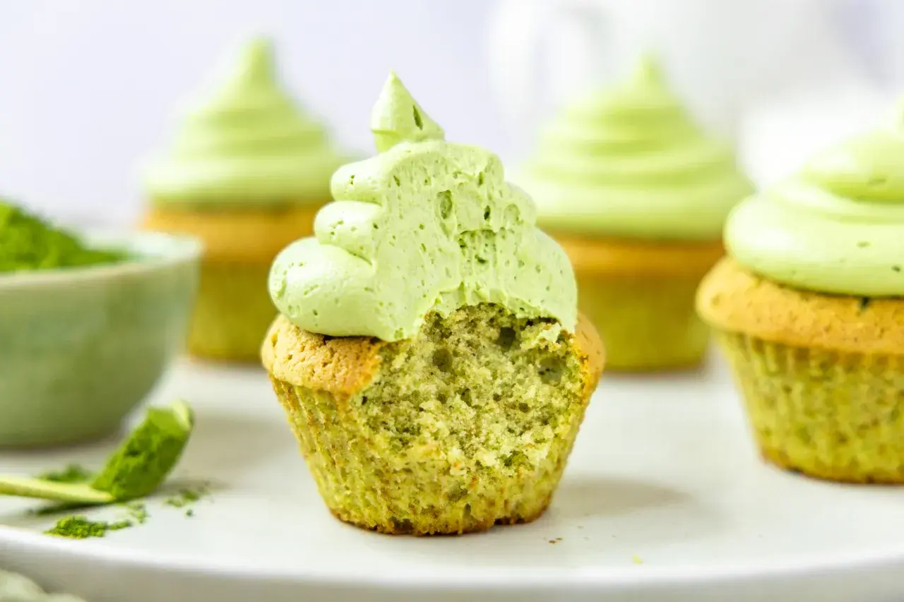 Saftige matcha cupcakes mit leuchtend grünem Topping. Ein Bissen fehlt, um die zarte Textur zu enthüllen.