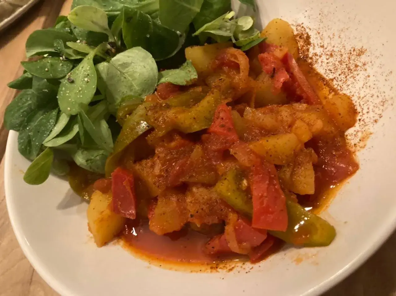 Un plat coloré de poivrons et pommes de terre mijotés, servi avec une salade verte. Une recette simple et savoureuse.
