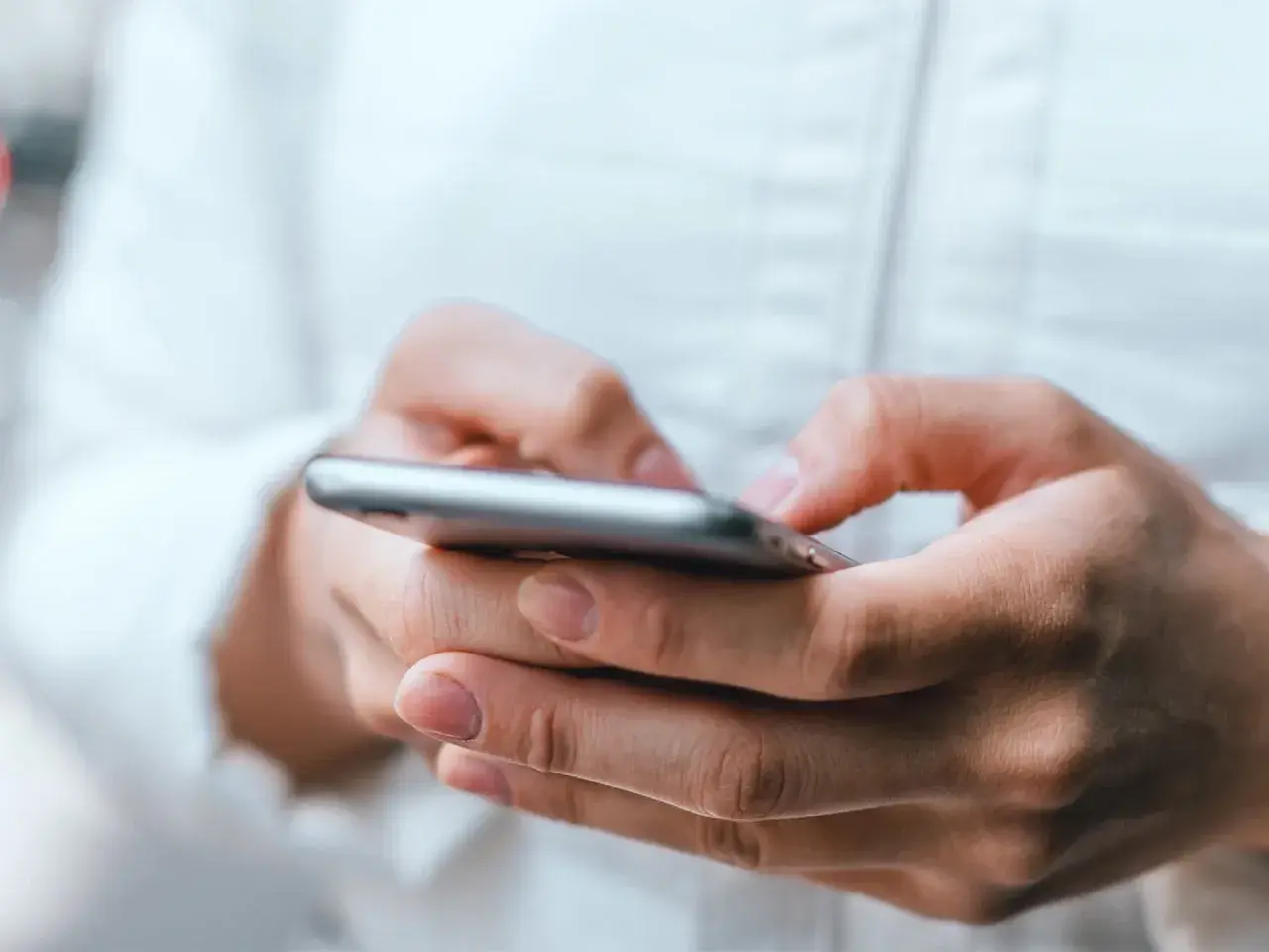 Dłonie trzymające smartfon, uważaj na oszustwa typu smishing, które mogą przyjść w każdej chwili.