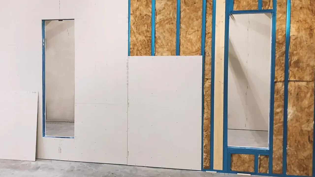Fase iniziale di come fare una parete in cartongesso: pannelli bianchi fissati su struttura metallica blu, con isolamento visibile.