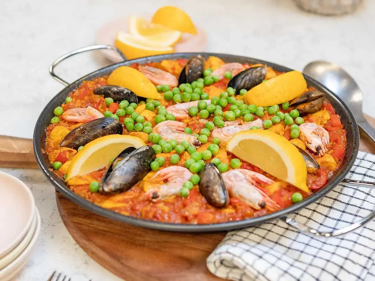 En stor paella med räkor, musslor, gröna ärtor och citronklyftor. Perfekt för ett somrigt paella recept.