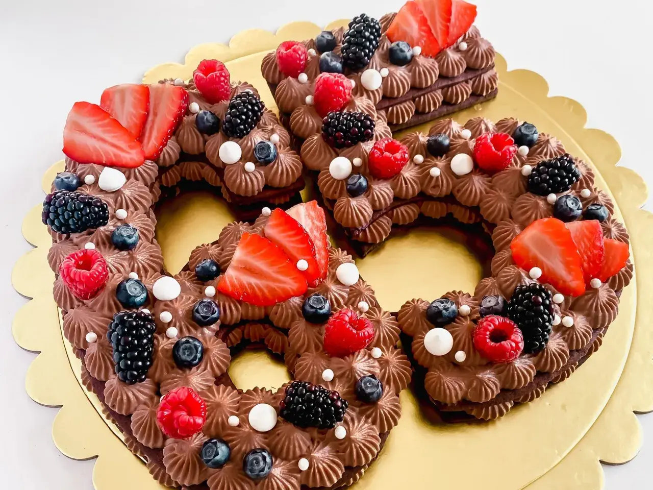 Una torta numero cioccolato, decorata con fragole, lamponi, mirtilli e more.