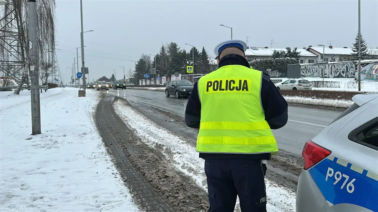 Policjant w kamizelce odblaskowej stoi przy drodze, gdzie kiedy zabierają prawko za prędkość. Śnieg i błoto na poboczu.