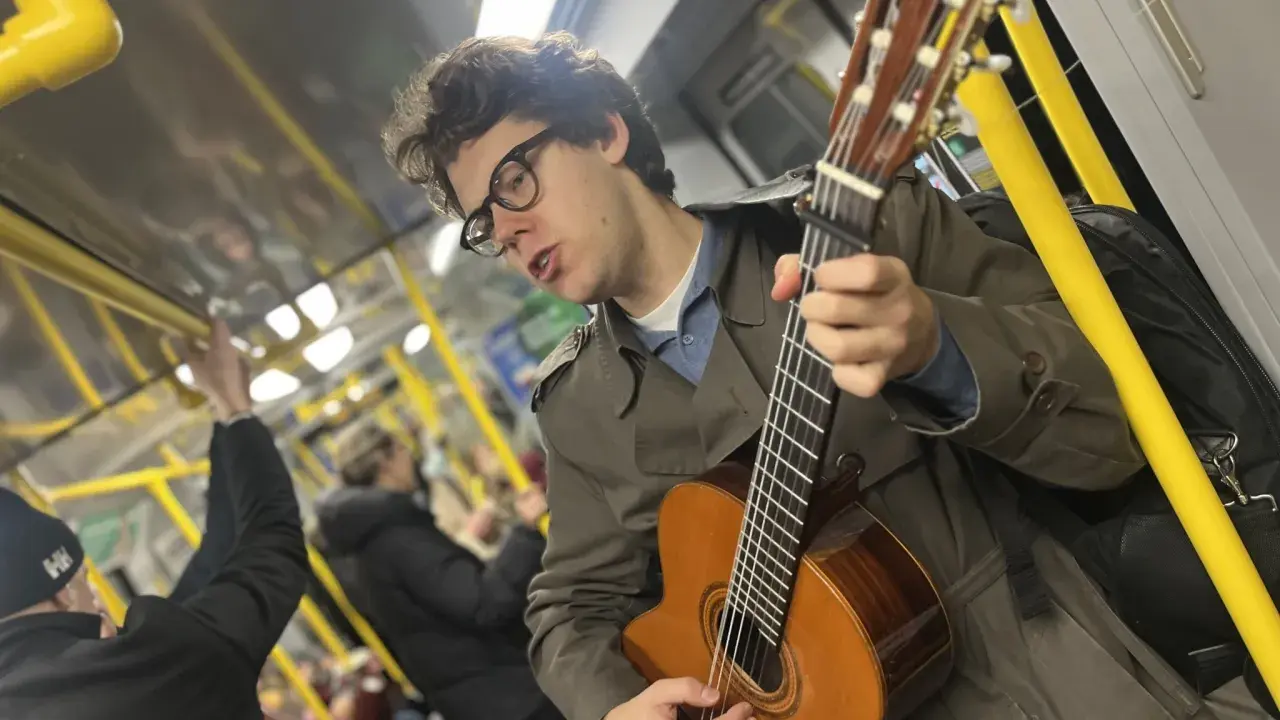 En ung man med glasögon spelar gitarr på tunnelbanan, en musikalisk själ med stockholm roots.