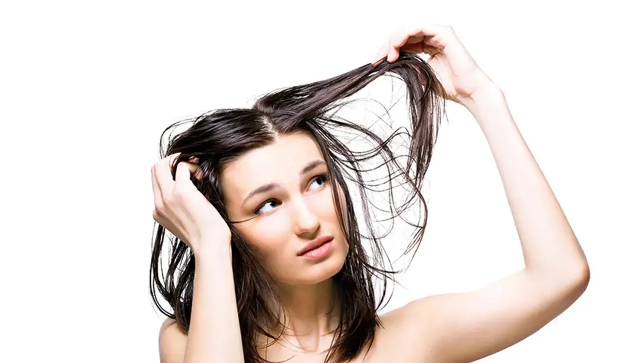 Mujer con cabello mojado, pensativa sobre lavarse el pelo todos los días.