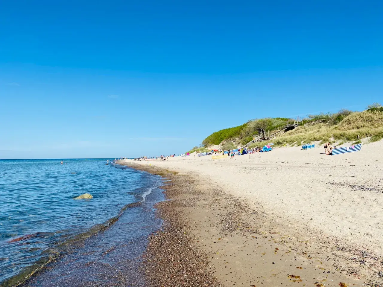 Sonniger Tag am Strand Nonnevitz. Menschen entspannen sich unter bunten Schirmen, während sanfte Wellen das Ufer erreichen.