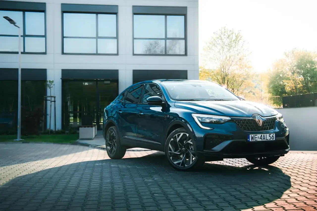 Elegancki, granatowy Renault Arkana na tle nowoczesnego budynku. Sprawdź, jaka jest jego renault arkana cena i możliwości.