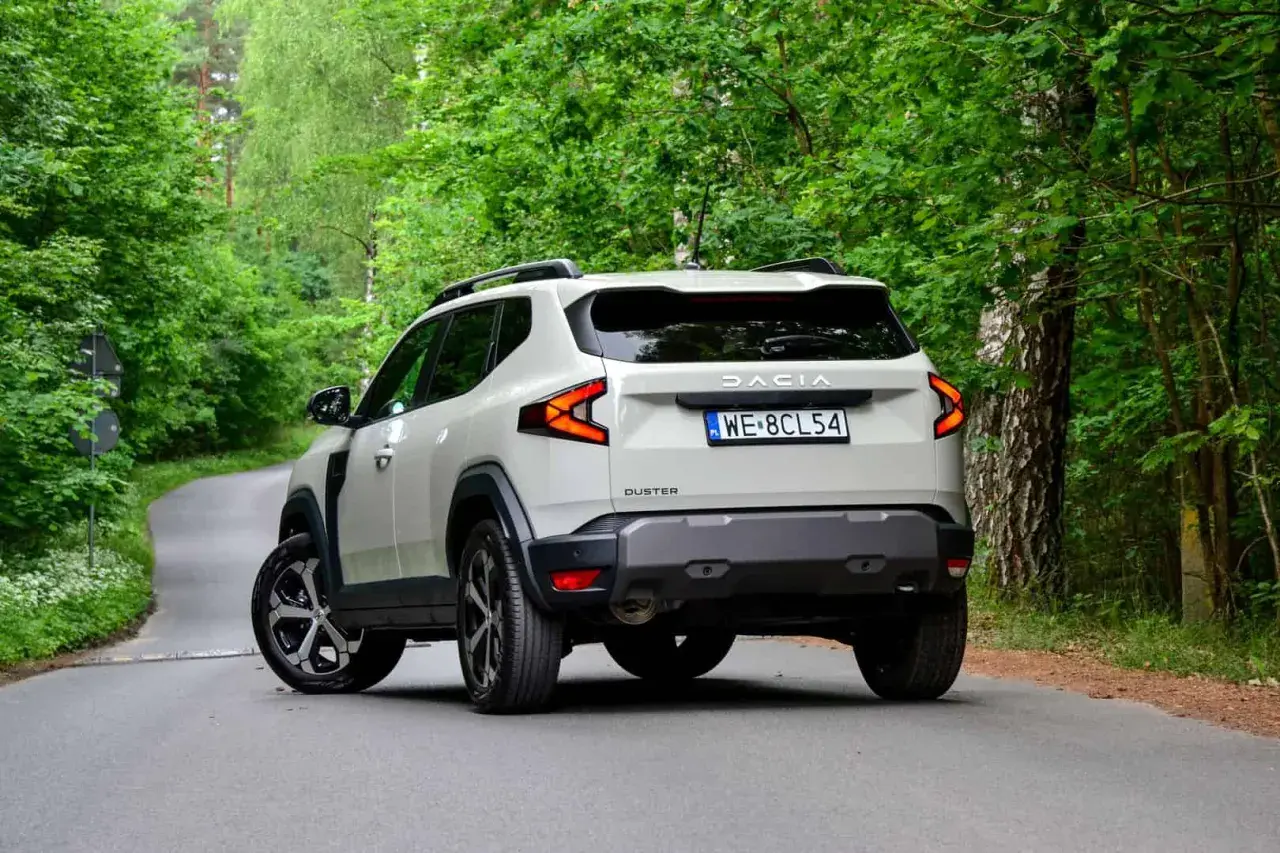 Nowy Dacia Duster 3 na krętej leśnej drodze. Nowoczesne światła i masywna sylwetka podkreślają jego terenowy charakter.