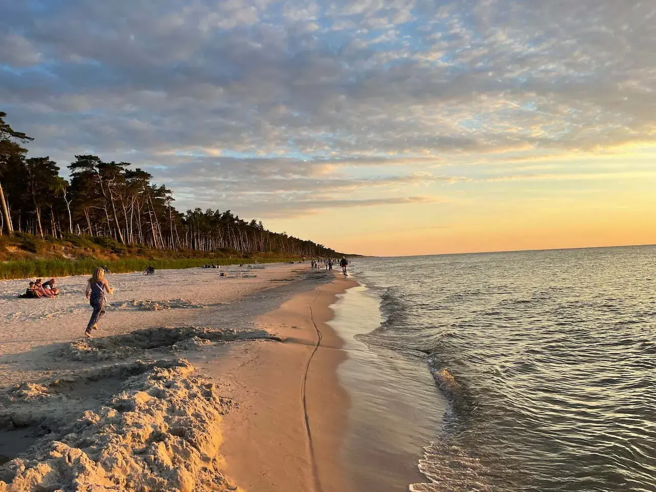 Piękny zachód słońca na plaży w Choczewie. Ludzie spacerują, a morze delikatnie faluje.