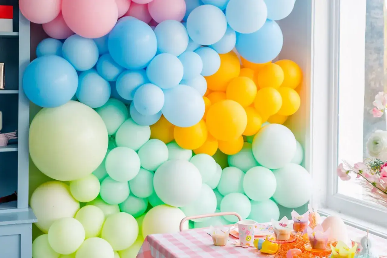 Kolorowa ściana z balonów: pastelowy róż, błękit, żółty i miętowy tworzą radosną oprawę dla świątecznego stołu.