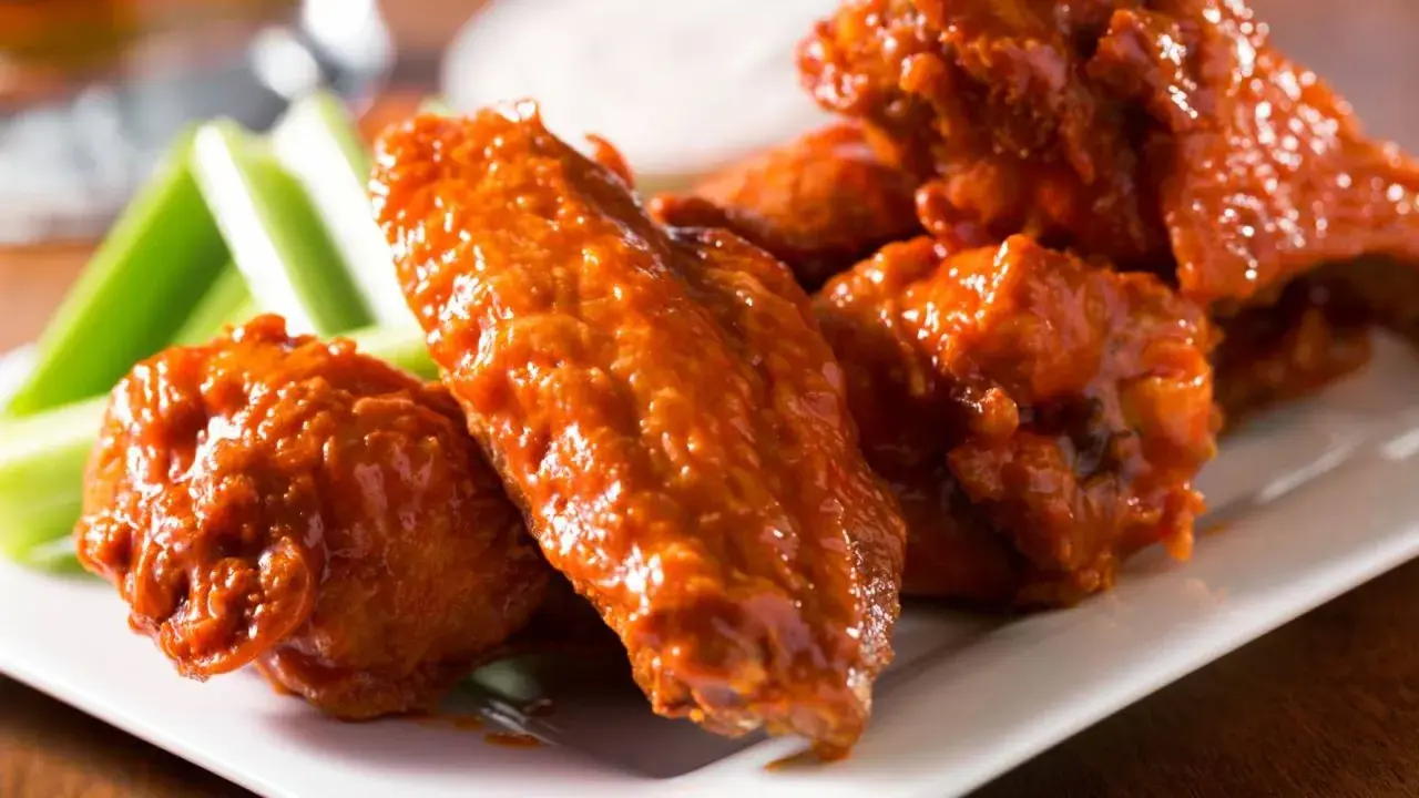 Un plato de alitas de pollo bañadas en salsa picante, acompañadas de bastones de apio fresco. ¡Un clásico irresistible!