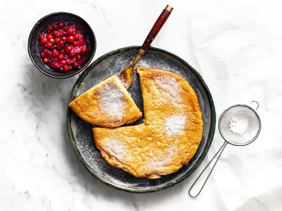 Puszysty omlet posypany cukrem pudrem, podany z żurawiną i łyżką.