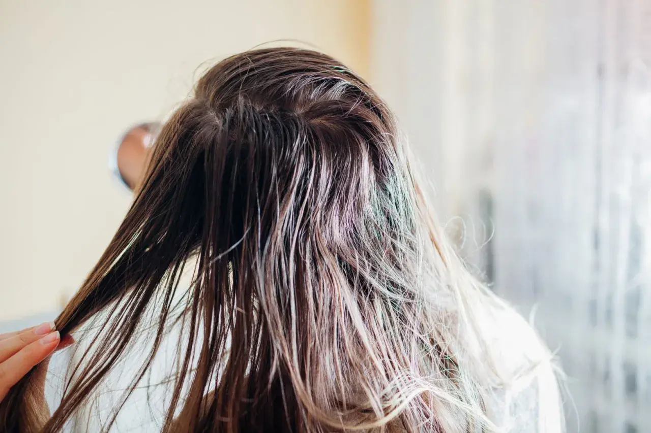 Nasse, braune Haare werden von einer Hand gehalten. Die Frau wäscht ihre **Haare nur mit Wasser**, um sie zu reinigen.