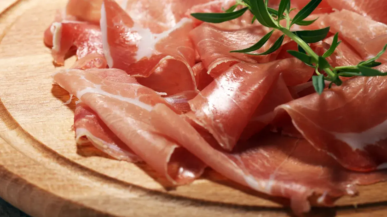 Cienkie plastry prosciutto crudo, ułożone na drewnianej desce, z gałązką rozmarynu. Pyszne, prawda?