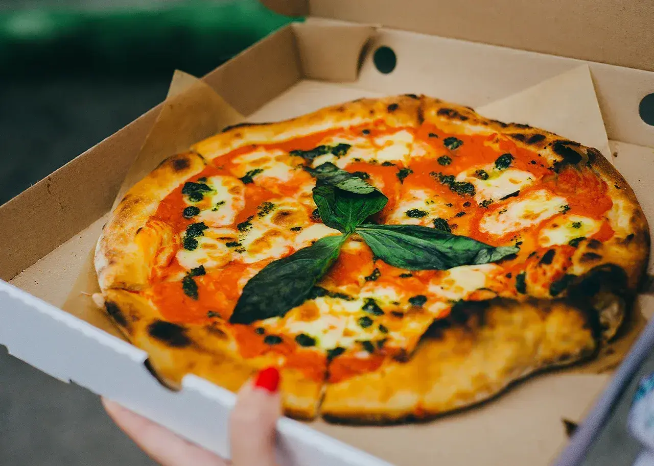 Pyszna pizza w kartonie na pizze, z sosem pomidorowym, mozzarellą i świeżą bazylią. Idealna na wynos!