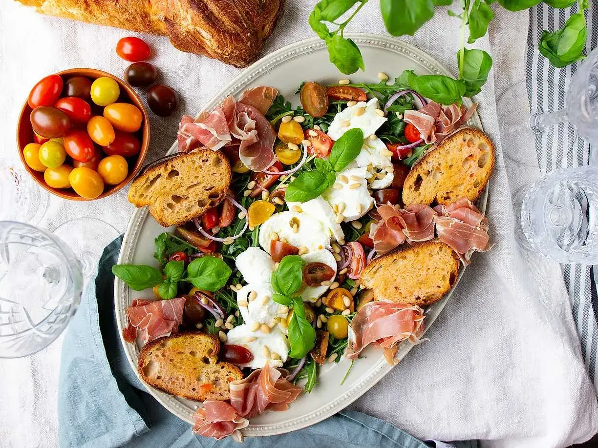 En härlig buffé med appertiff mat: mozzarella, tomater, prosciutto, ruccola och rostat bröd. Perfekt för en somrig förrätt.