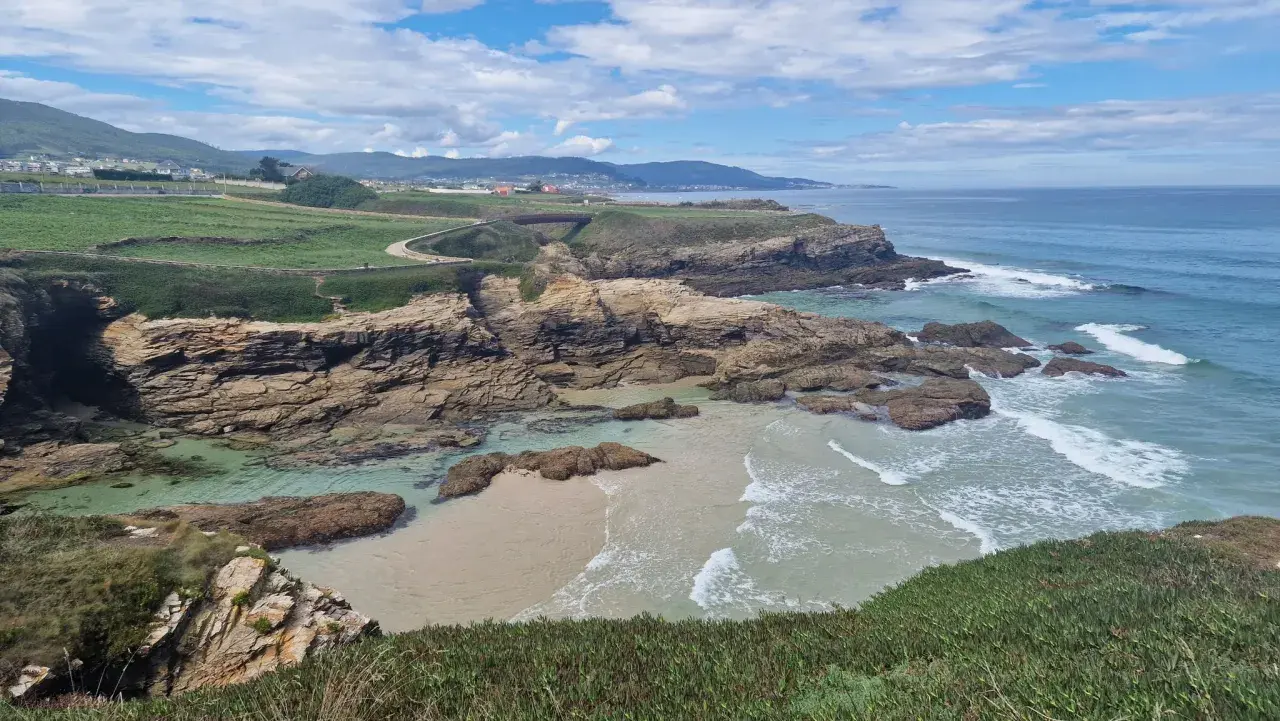 Senderistas disfrutan de las impresionantes rutas senderismo Foz, con acantilados rocosos, playas de arena y el mar azul.