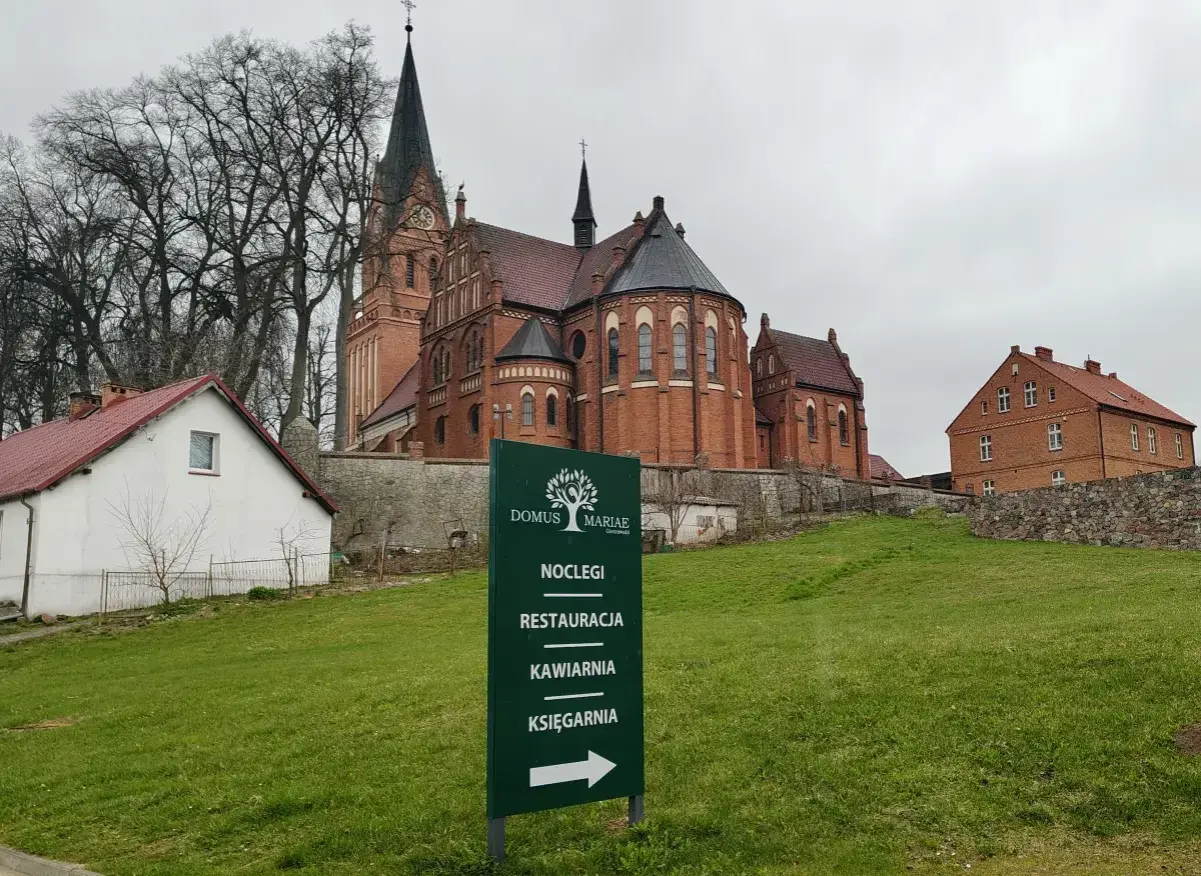 Dom Pielgrzyma w Gietrzwałdzie oferuje noclegi, restaurację, kawiarnię i księgarnię. W tle kościół.