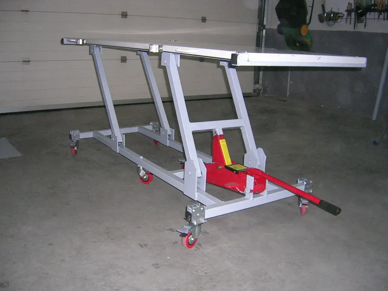 Elevador moto casero con gato hidráulico rojo, estructura metálica gris y ruedas. Ideal para reparaciones.