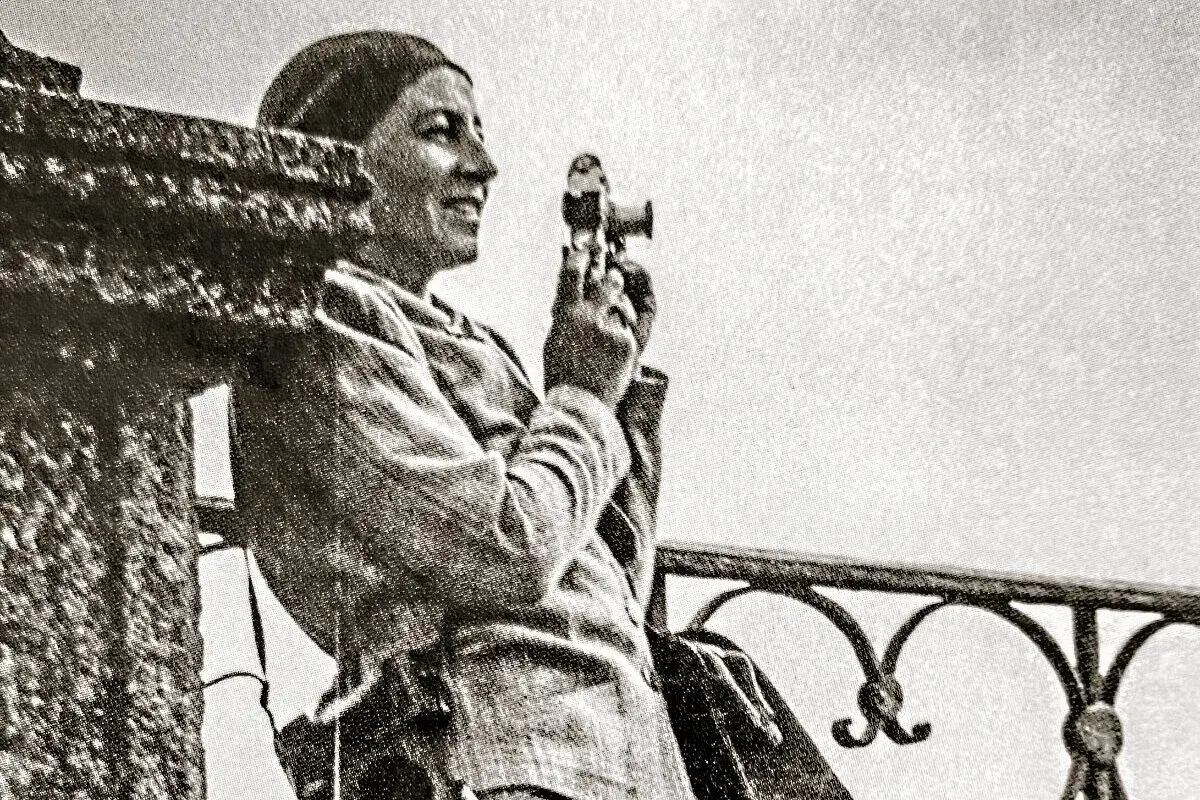 Zofia Chomętowska, z aparatem w dłoni, patrzy w dal. W tle balustrada i jasne niebo.