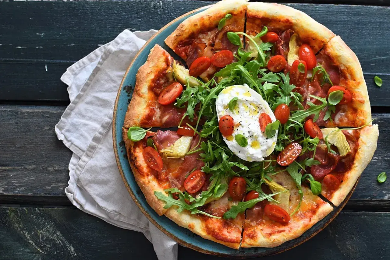Pizza z mortadelą, rukolą, pomidorkami i burratą na niebieskim talerzu.