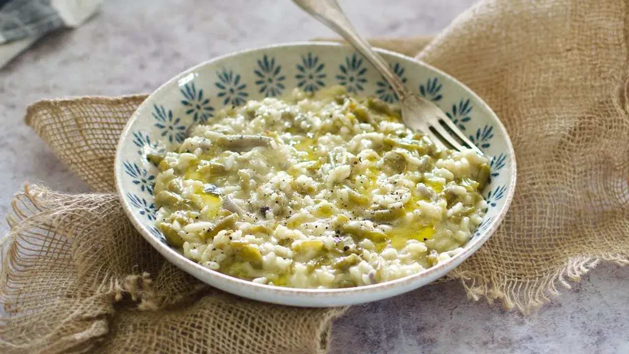 Un cremoso risotto con fagiolini, condito con olio d'oliva e pepe nero, servito in una ciotola decorata.