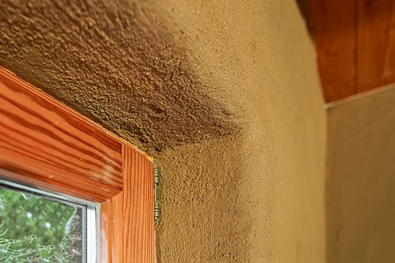 Lehmputz nachteile: raue Textur, die Schmutz anziehen kann, um ein Fenster mit Holzzarge und sichtbarem Putz.