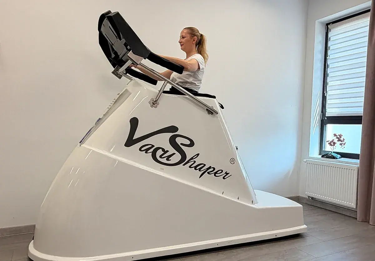 Kobieta ćwiczy na urządzeniu Vacu Shaper, które pomaga w modelowaniu sylwetki.