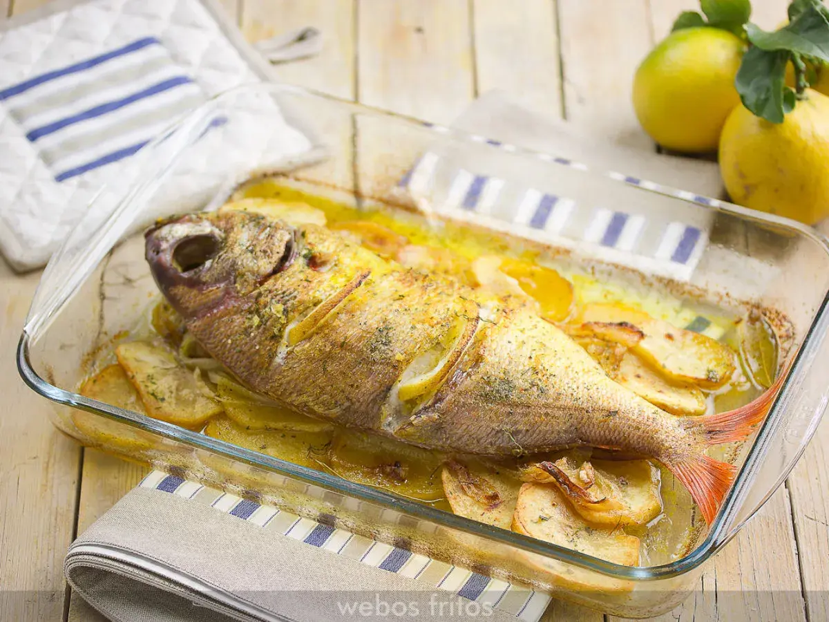 Besugo al horno con patatas y limón, recién sacado del horno en una fuente de cristal.