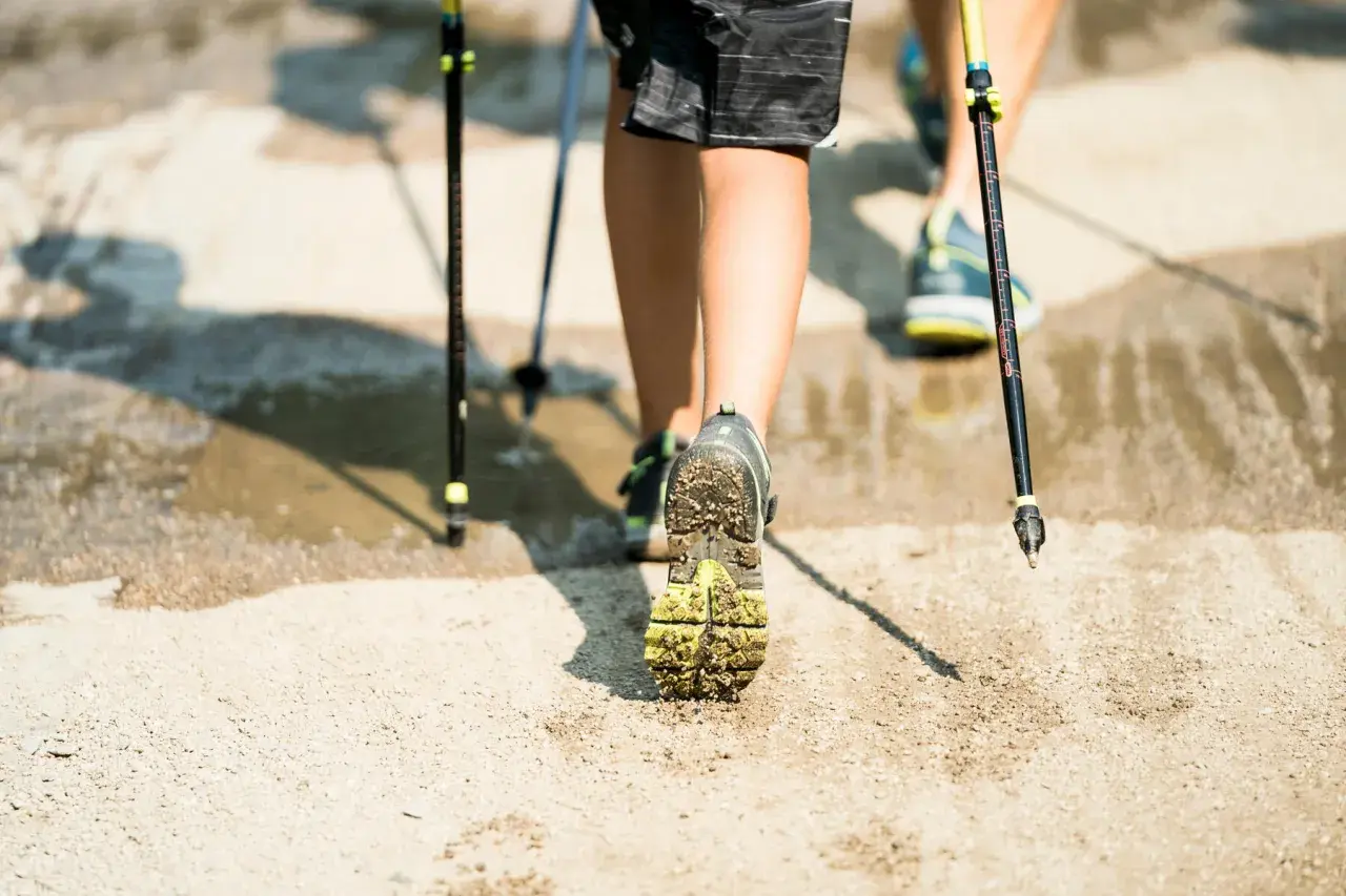 Nordic walking - jak chodzić, żeby schudnąć. Dwie osoby maszerują z kijkami po wilgotnym, piaszczystym podłożu.