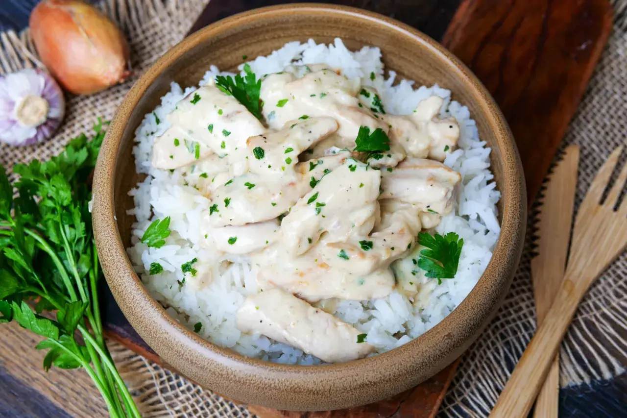 Schmackhaftes Puten Geschnetzeltes in cremiger Sauce auf Reis, garniert mit Petersilie. Daneben Zwiebel und Knoblauch.