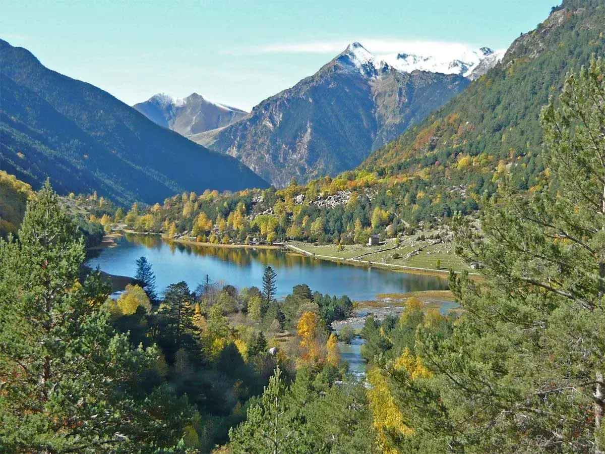 El estany de Llebreta, un lago alpino rodeado de bosques otoñales y montañas nevadas, ofrece una vista serena y colorida.
