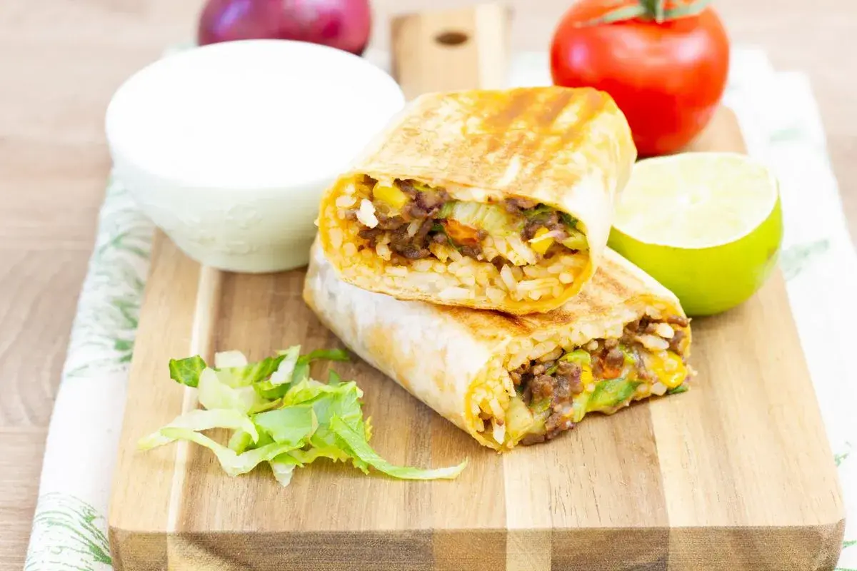 Pyszny burrito przepis: dwa połówki burrito z ryżem, mięsem mielonym, kukurydzą i warzywami, podane z limonką i śmietaną.