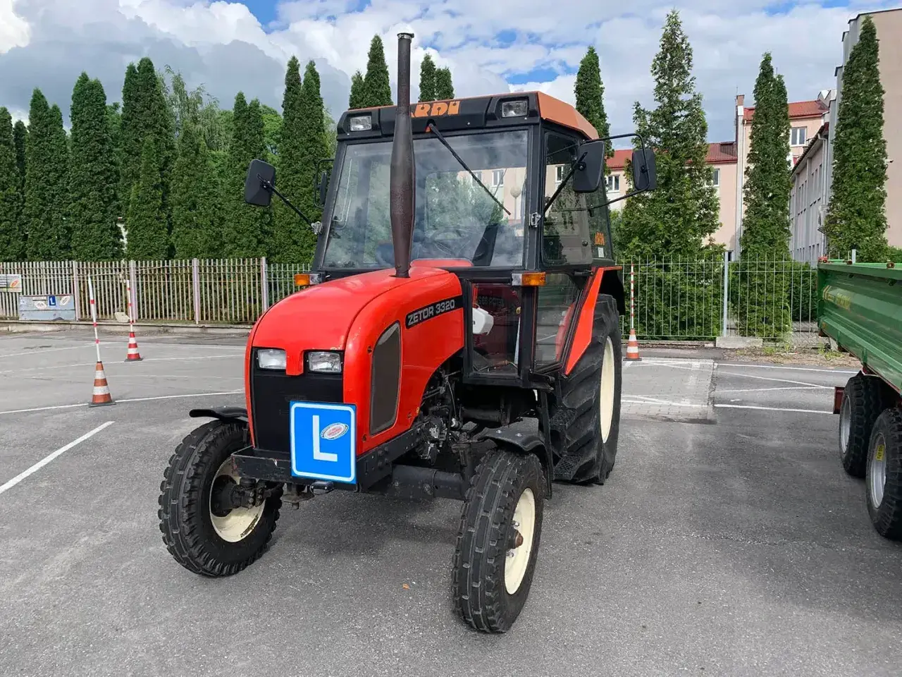 Czerwony traktor Zetor z literą "L" na niebieskiej tablicy, symbolizujący naukę jazdy. Kategoria t prawo jazdy.