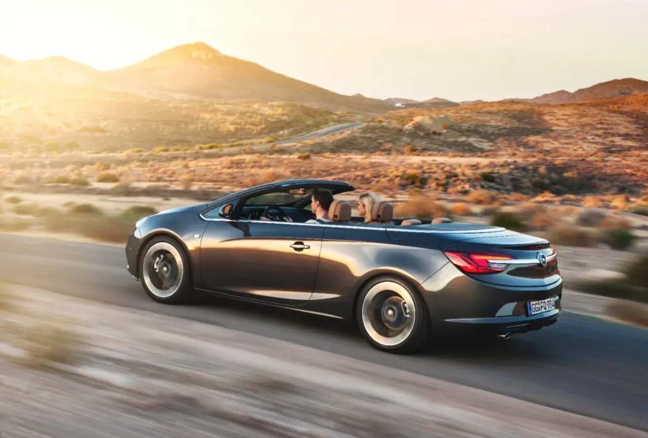 Para podróżuje kabrioletem Opel Cascada przez pustynny krajobraz o zachodzie słońca.