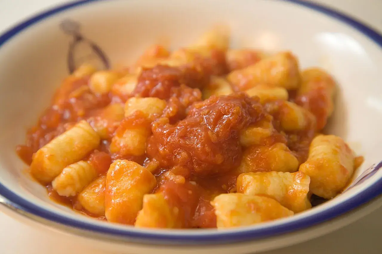 Pyszne gnocchi alla sorrentina w sosie pomidorowym, podane w białej misce z niebieskim rantem.