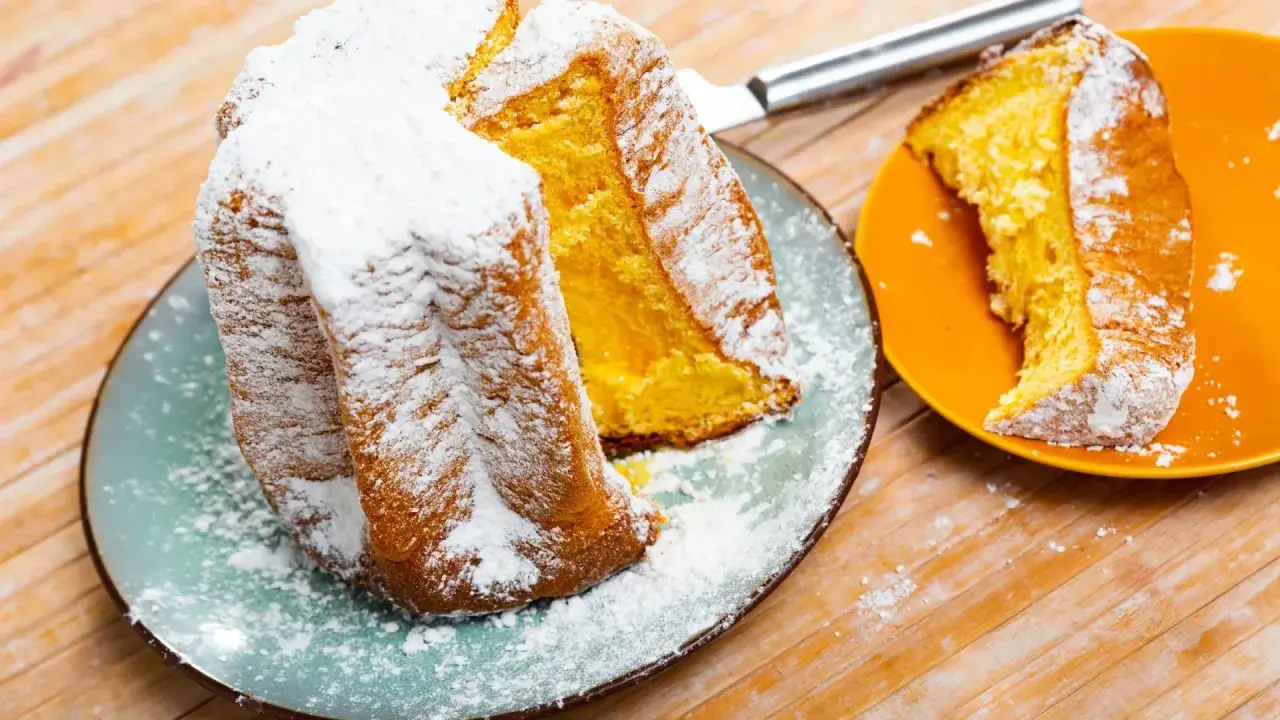 Une brioche italienne pandoro, saupoudrée de sucre glace, est servie sur une assiette bleue. Une part est sur une assiette orange.