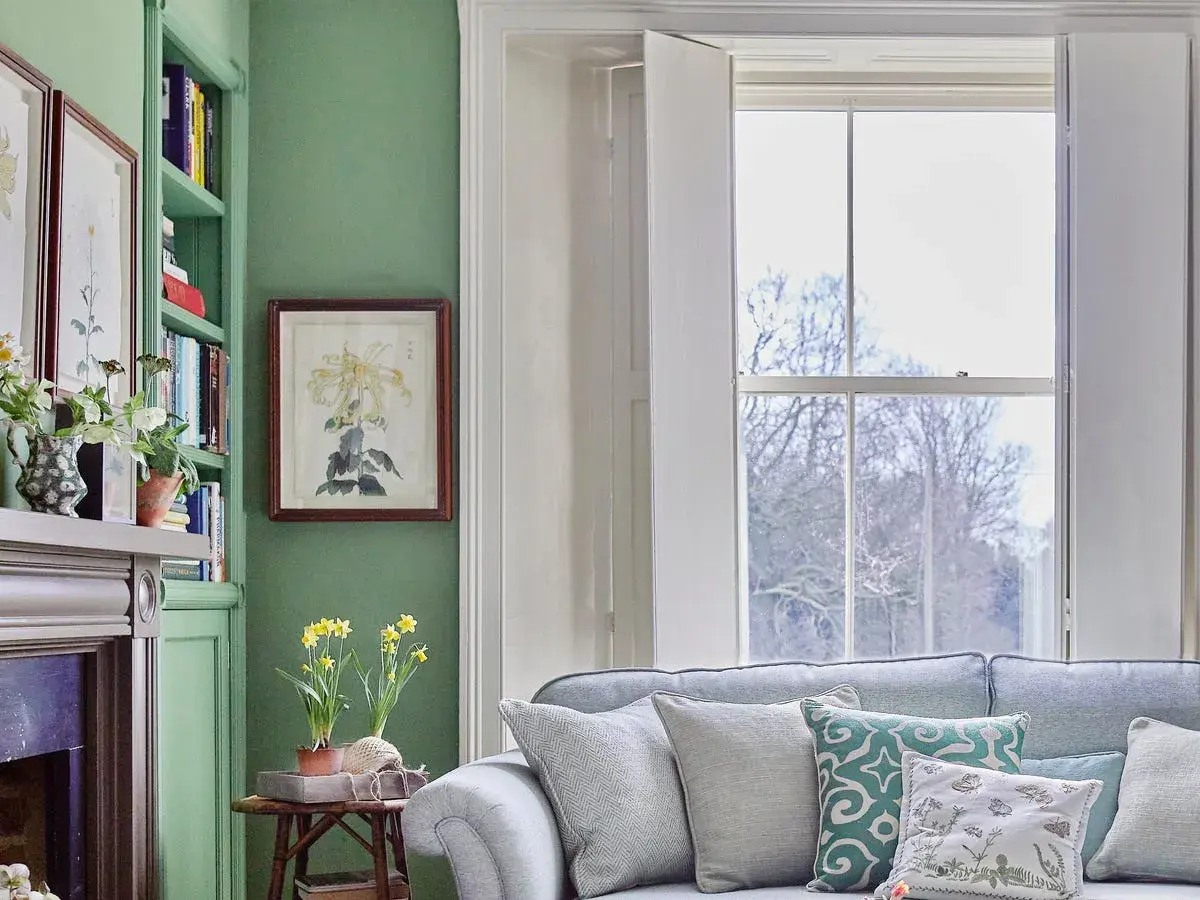 A cozy living room with country contemporary furniture, featuring a green bookshelf, fireplace, and a plush sofa adorned with patterned pillows.