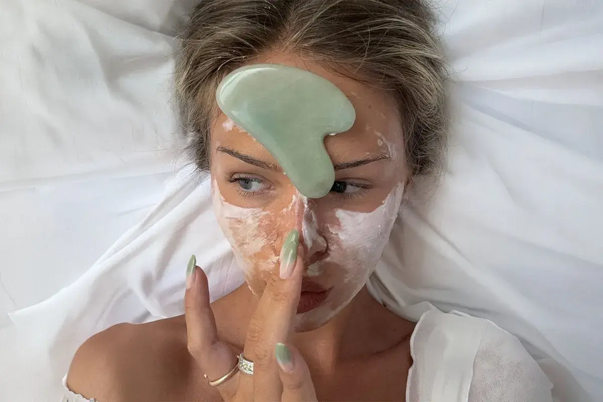 En kvinna med ansiktsmask och en grön sten för ansikts massage.