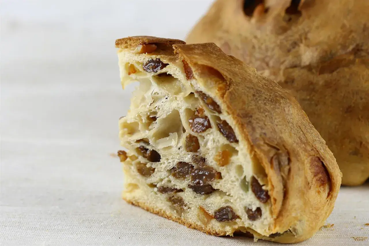 Fetta di pandolce genovese ricetta originale, con uvetta e canditi, su sfondo chiaro.