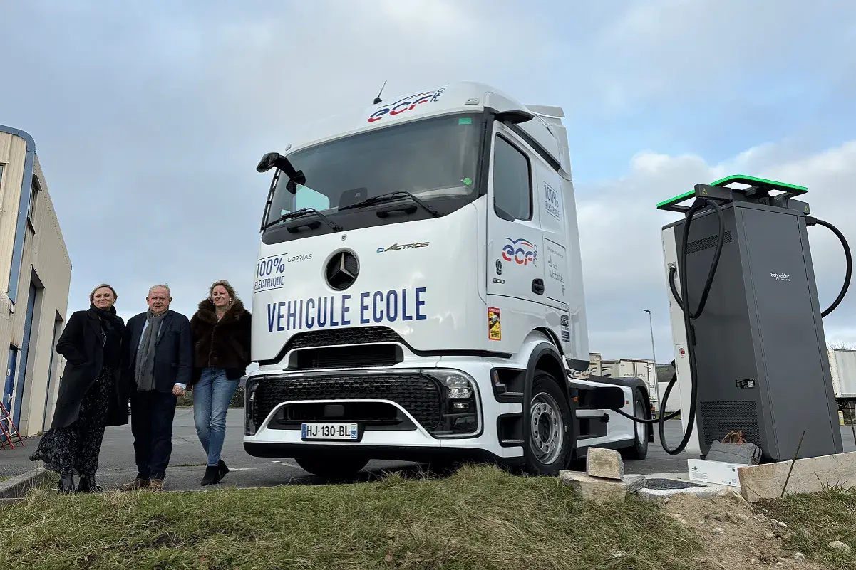 Trois personnes posent devant un camion école 100% électrique, prêt à être rechargé. L'avenir des camions électriques est en marche.