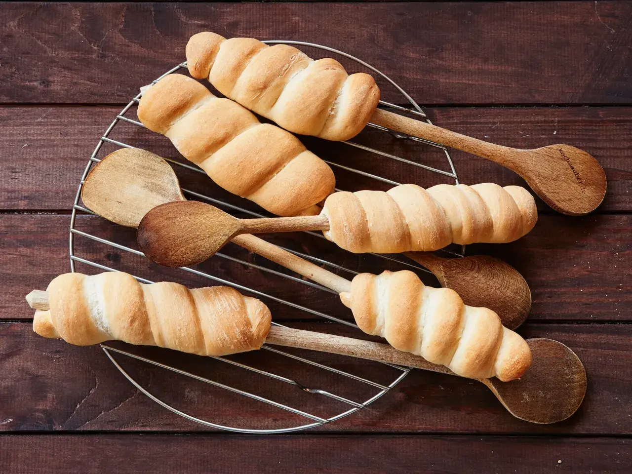 Frisch gebackenes Stockbrot mit frischer Hefe, auf Holzkochlöffeln auf einem Gitterrost arrangiert.